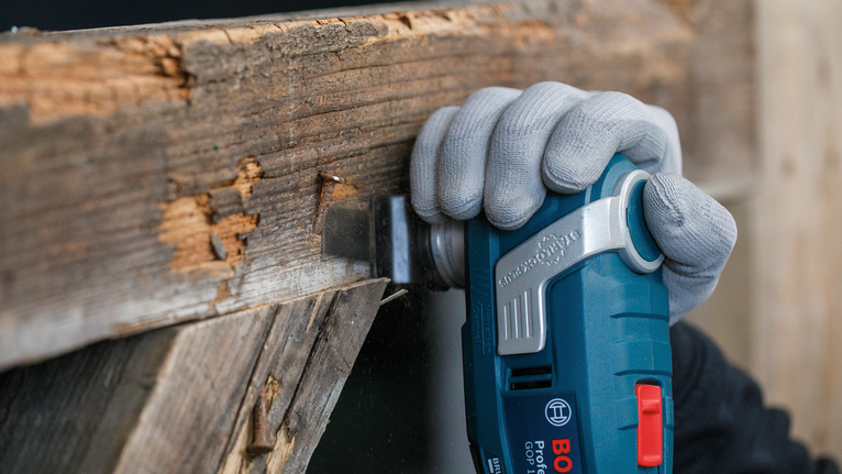 Person wearing safety equipment sands rough wood with a blue oscillating multi-tool.