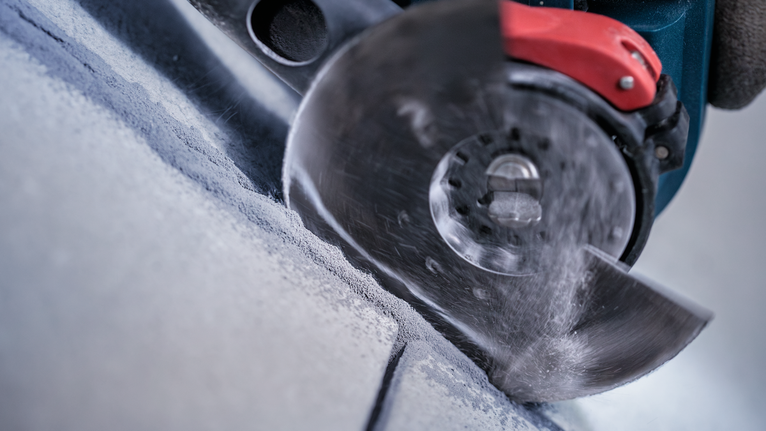 Rotary saw blade cutting into concrete, producing dust.