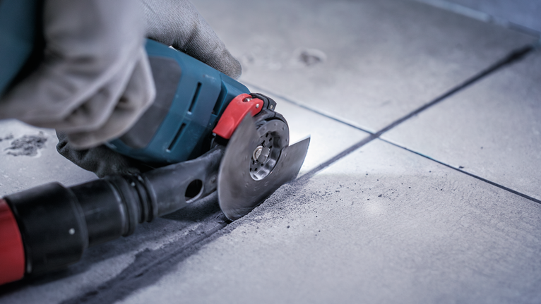 Person wearing safety equipment cuts a tile with an angle grinder.