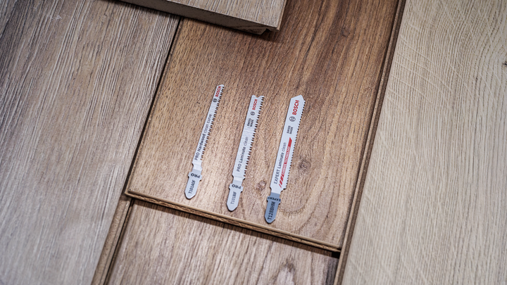 Four jigsaw blades of varying sizes arranged on wooden flooring.