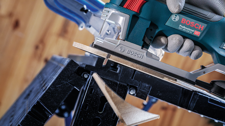 Person wearing safety equipment uses a jigsaw to cut a piece of wood.