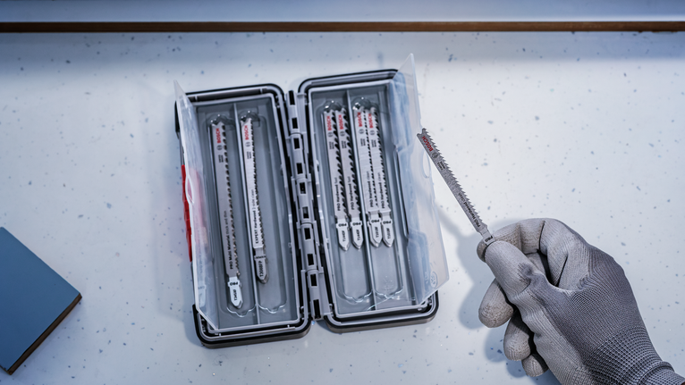 Person wearing safety equipment selects a saw blade from a plastic storage case.