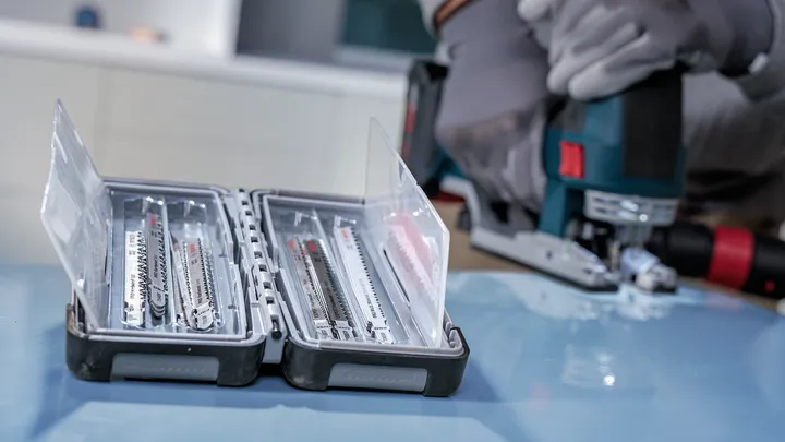 Person wearing safety equipment uses a jigsaw near an open case of saw blades.