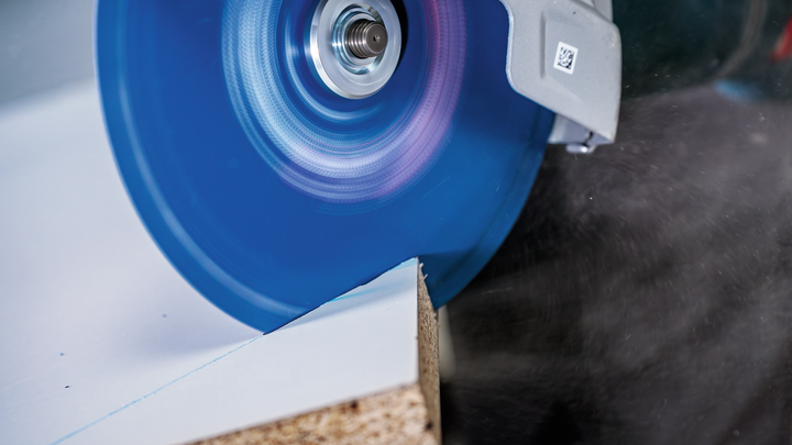 Circular saw blade cutting through a laminated wooden board.
