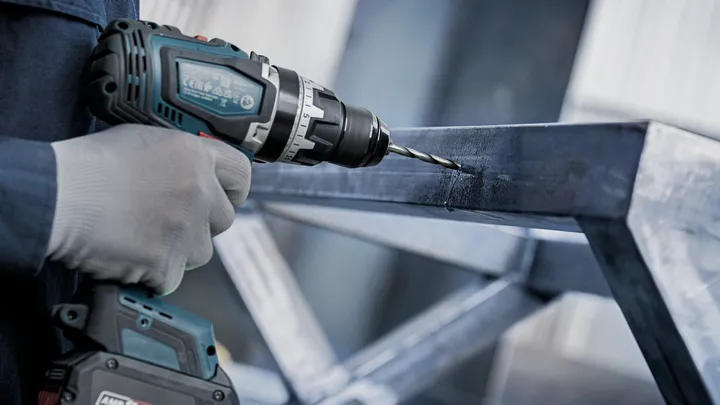 Person wearing safety equipment drills into a metal frame.