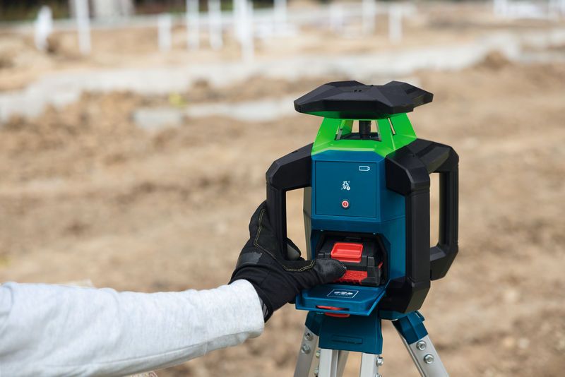 Person wearing safety equipment operates a laser leveling tool on a construction site.