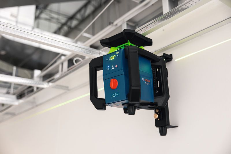 Laser leveling tool mounted on a wall projects a green alignment line in an industrial setting.