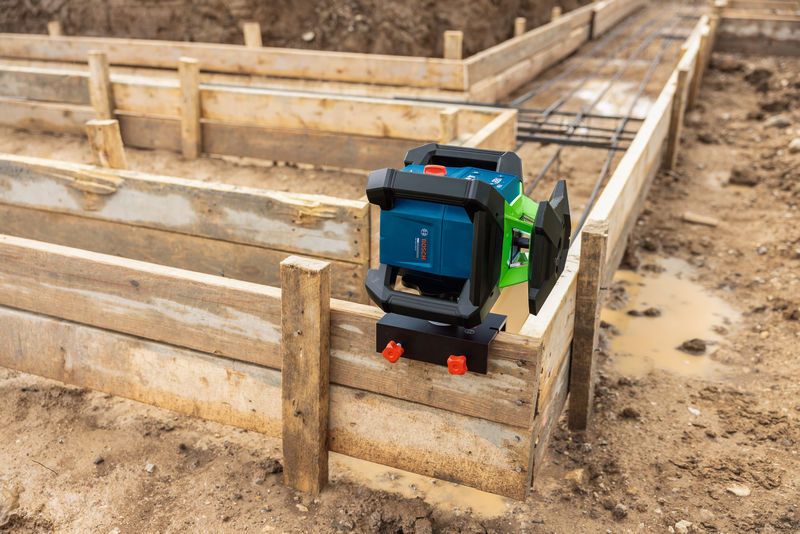 Laser leveling tool with bracket and mount attached to wooden formwork at a construction site.