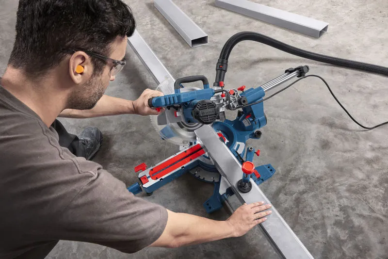 Person wearing safety equipment cuts metal tubing with a mitre saw on a workshop floor.