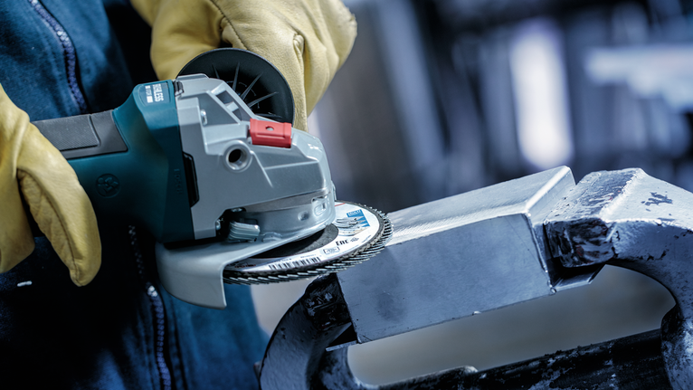 Person wearing safety equipment uses an angle grinder to cut a metal block.