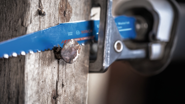 Saw blade cutting through a wooden beam with a metal nail embedded.