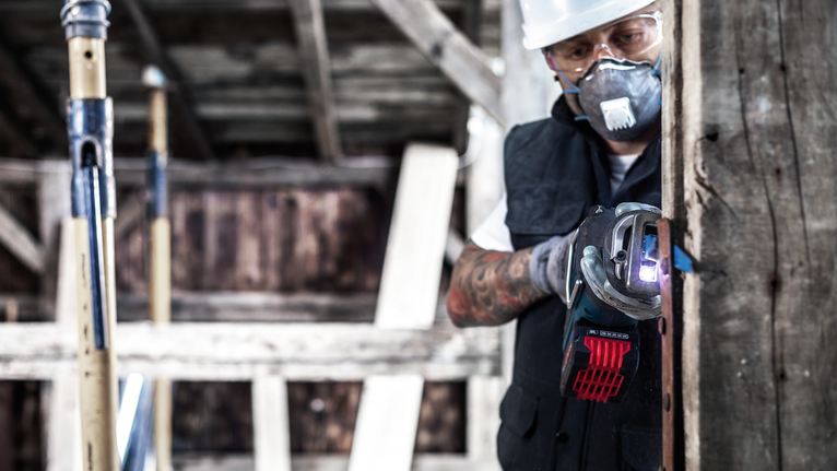 Person wearing safety equipment uses a power tool to cut through a wooden beam.