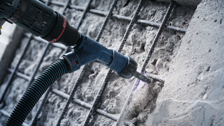 Rotary hammer drilling concrete near exposed rebar, dust being extracted.