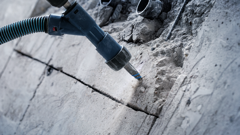 A rotary hammer drills into concrete at a construction site.