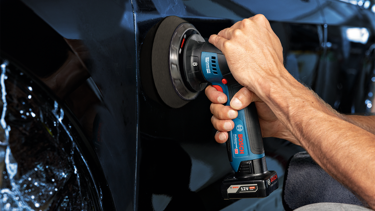 Person polishing a black car door with a cordless power tool.