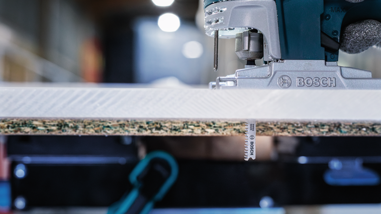 A jigsaw cutting through a laminated wood panel in a workshop.
