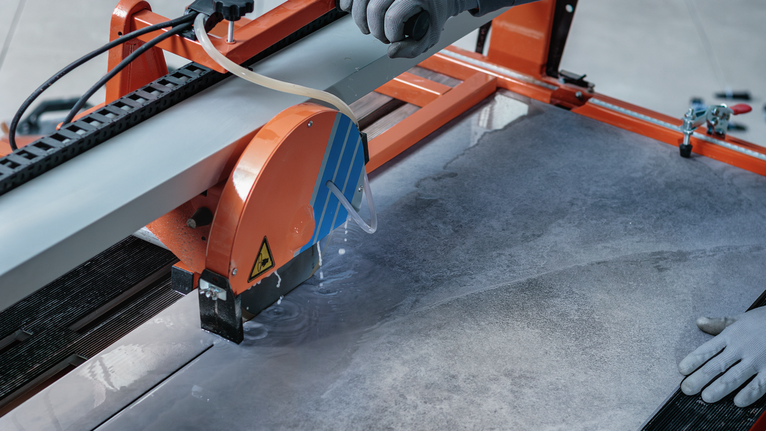 Person wearing safety equipment cuts a large tile with a wet tile saw.