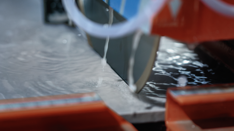 Wet saw blade cutting through a slab of stone with water cooling the surface.
