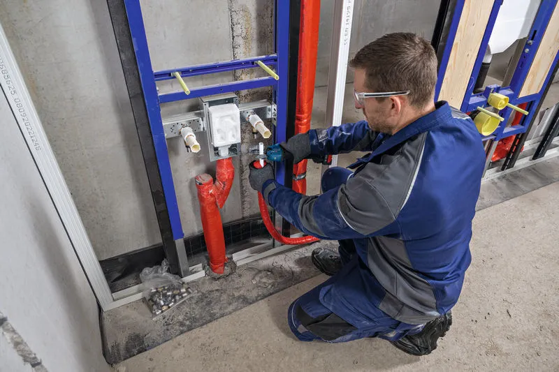 A worker wearing safety equipment uses a cordless pipe shear to cut a red pipe.