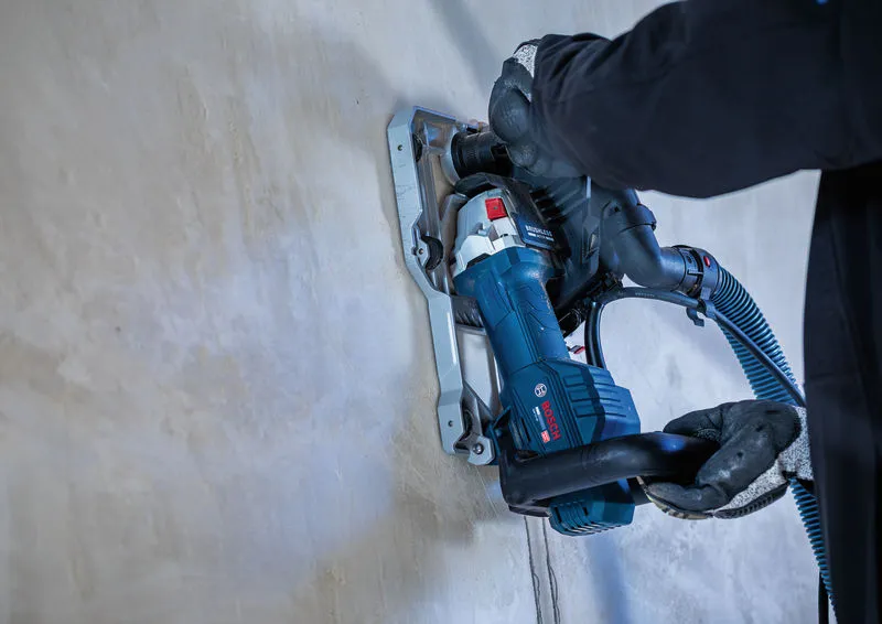 A person wearing safety equipment uses a wall chaser to cut a groove in a concrete wall.