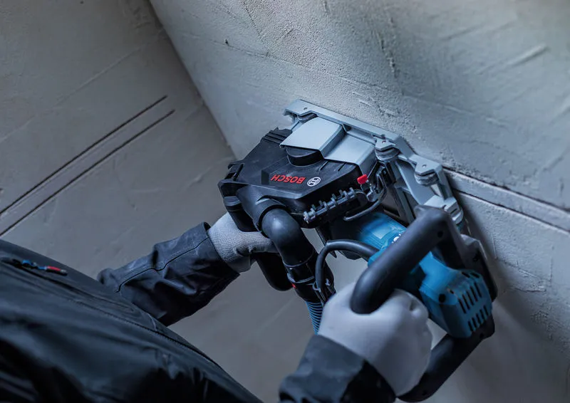A person wearing safety equipment uses a wall chaser to cut grooves in a plaster wall.