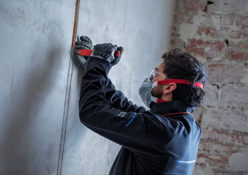 A person wearing safety equipment creates a channel in concrete with a wall chaser.