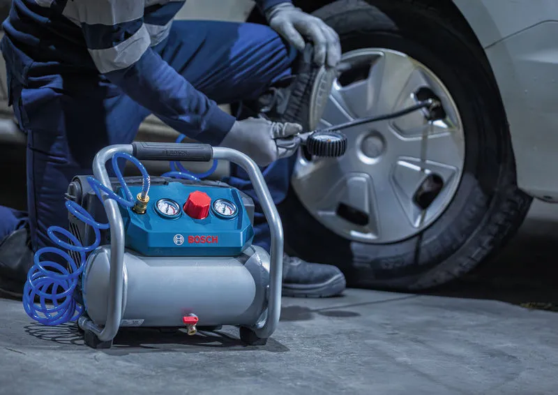 A person wearing safety equipment uses an air compressor to clean a car wheel.
