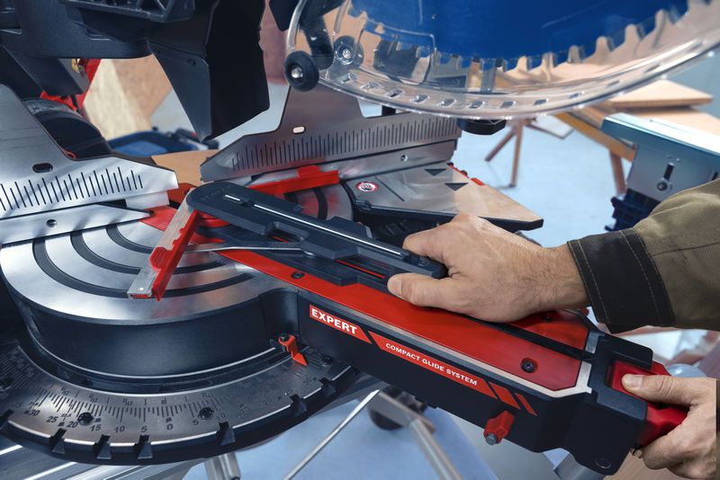 A person adjusts a mitre saw in a workshop setting.
