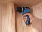 A person uses a cordless impact drill driver to assemble a wooden cabinet.