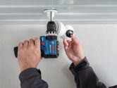 A person using a cordless drill to install a security camera on the ceiling.
