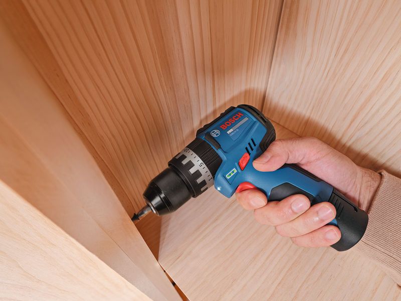 A person uses a cordless impact drill to drive a screw into a wooden surface.