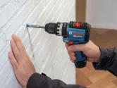 A person drills into a white brick wall using a cordless impact drill.