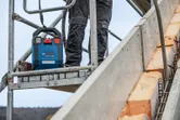 A person wearing safety equipment stands on scaffolding next to a portable power unit.