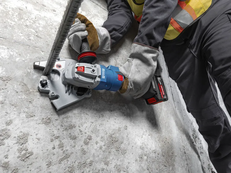 A person wearing safety equipment uses a cordless rebar cutter on a concrete floor.
