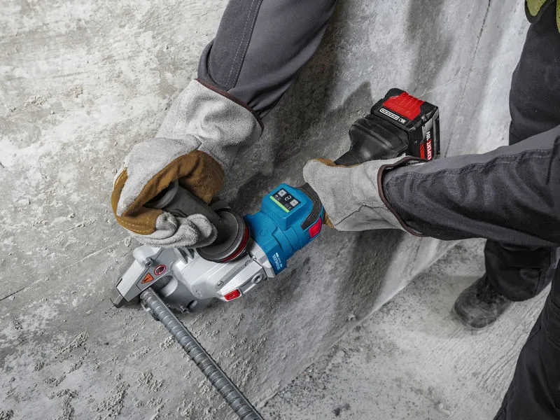 A person wearing safety equipment uses a cordless tool to cut rebar next to a concrete wall.