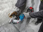 A person wearing safety equipment uses a cordless tool to cut rebar next to a concrete wall.