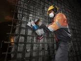 A worker wearing safety equipment cuts rebar on a construction site using a cordless rebar cutter.
