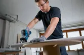 A person wearing safety equipment cuts a metal pipe with a power saw.