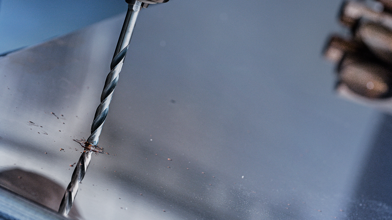 Person using a drill to make a hole in a metal sheet.
