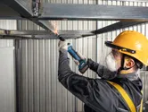 A person wearing safety equipment uses a cordless straight grinder to grind a metal beam.