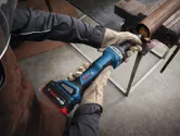 A person wearing safety equipment grinds a metal pipe using a cordless straight grinder.