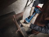 A person wearing safety equipment grinds a metal beam with a cordless straight grinder.