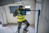 A person wearing safety equipment drills into a concrete wall with a rotary hammer.