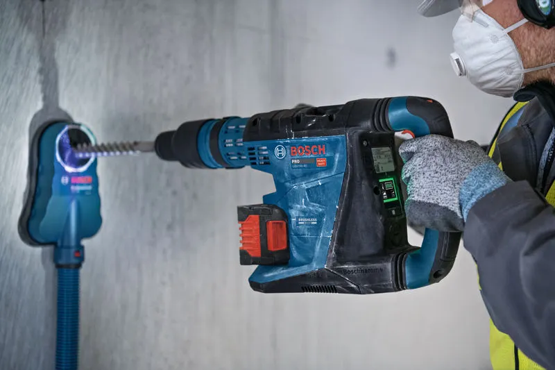 A person wearing safety equipment uses a rotary hammer to drill into a concrete wall.