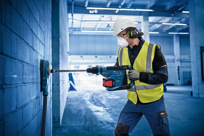 A person wearing safety equipment drills into a brick wall with a cordless rotary hammer.