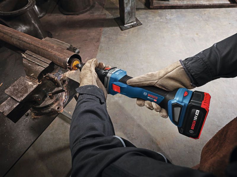 A person wearing safety equipment grinds the inside of a metal pipe with a cordless tool.