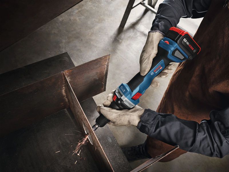 A person wearing safety equipment grinds metal with a cordless straight grinder.