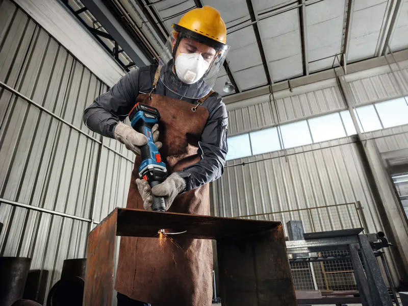 A person wearing safety equipment uses a cordless straight grinder on a metal beam.