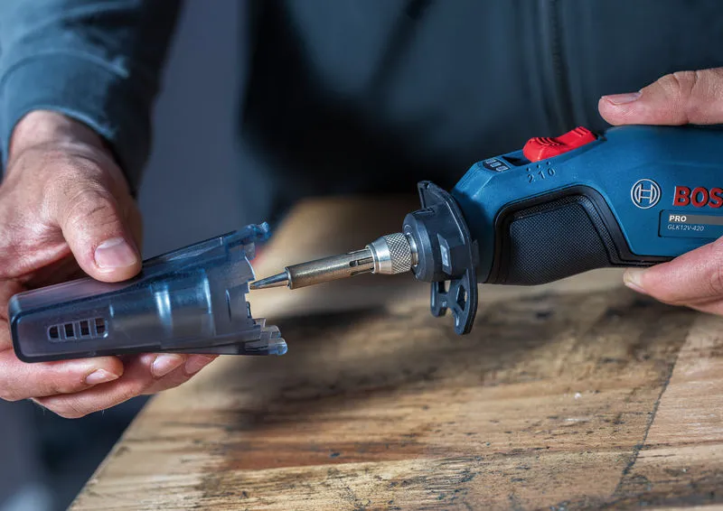 A person holds a cordless soldering iron with a protective cap on a wooden table.