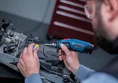 A person wearing safety equipment solders wires with a cordless soldering iron.